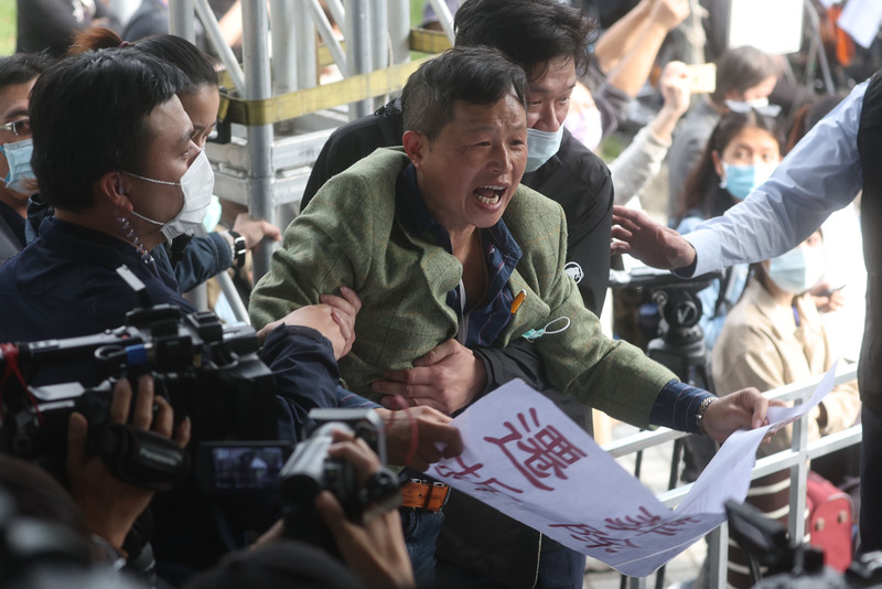 台灣國理事長陳峻涵（中綠衣者）持 標語到場抗議，遭現場人員拉住制止。 中央社
