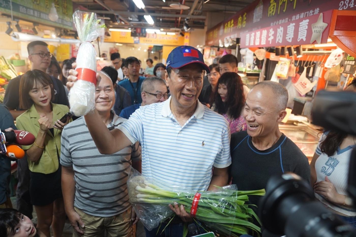 鴻海創辦人郭台銘(中)今參訪南門市場，受到攤商熱情歡迎，有人送他青蒜表達支持。中央社