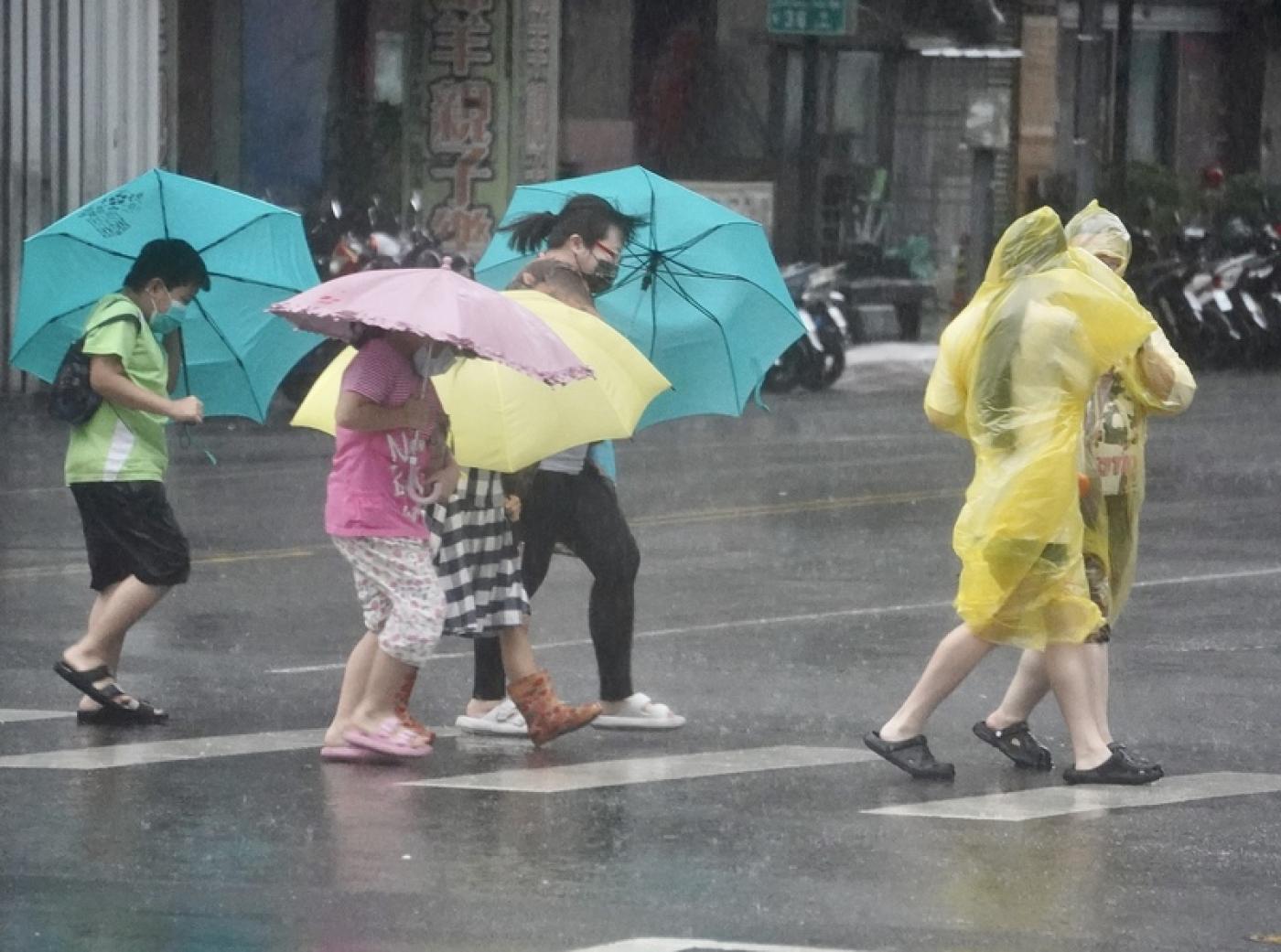 山陀兒颱風來襲，街頭民眾穿著雨衣、撐傘在強風雨勢中前行。 中央社